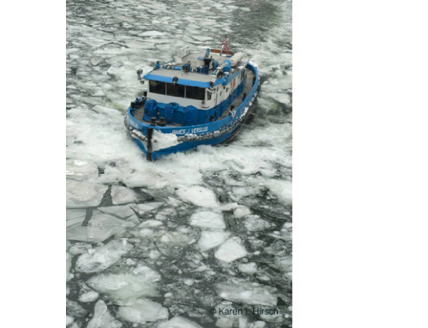 Blue and white boat cutting through ice on the Chicago River.